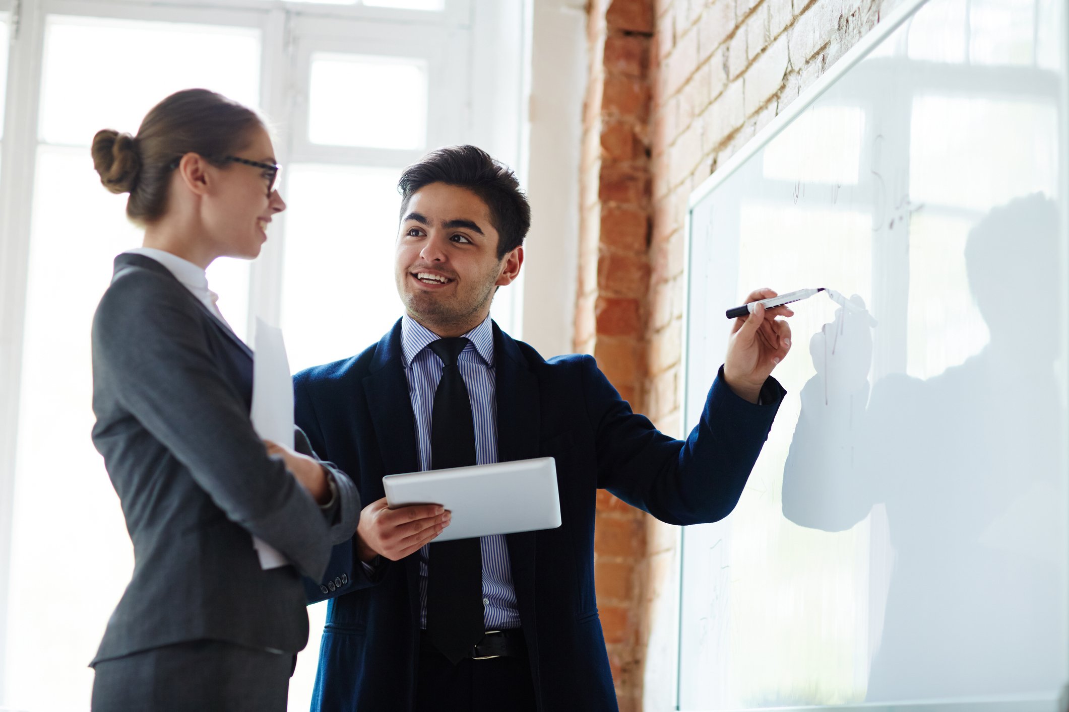 A man and women in suits planning on a dry-erase board.